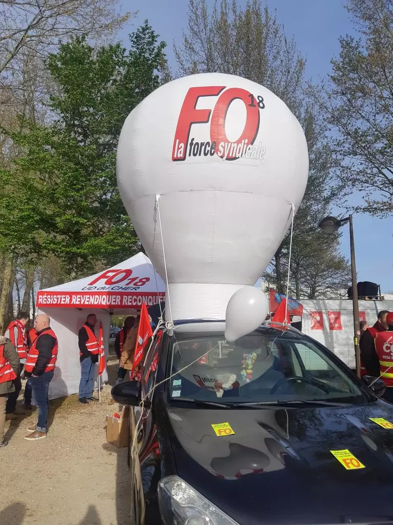 montgolfière gonflable blanche FO 18 accroché à une voiture pendant une manifestation